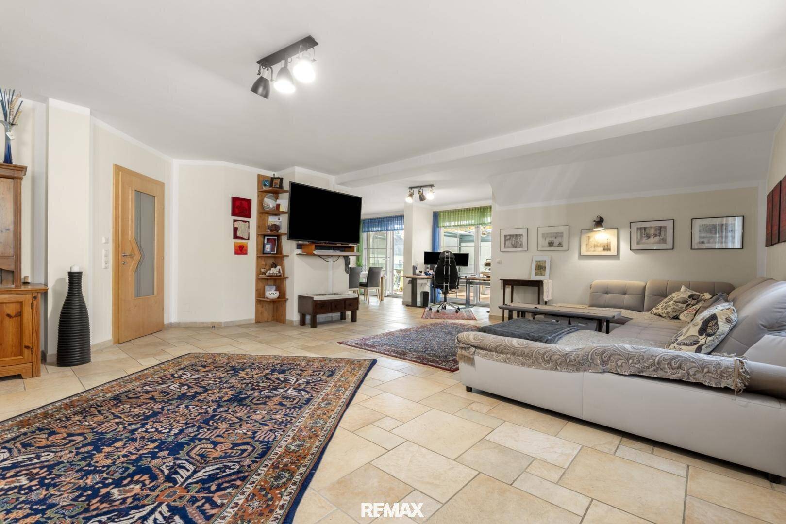 Geräumiges Wohnzimmer mit Fliesenboden, großem Sofa und Blick auf den angrenzenden Essbereich.