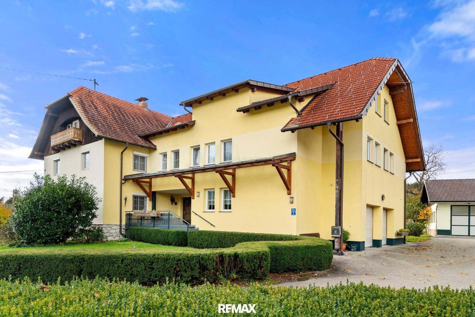 Ansicht des Haupthauses mit gelber Fassade, rotem Ziegeldach und einem gepflegten Vorgarten.