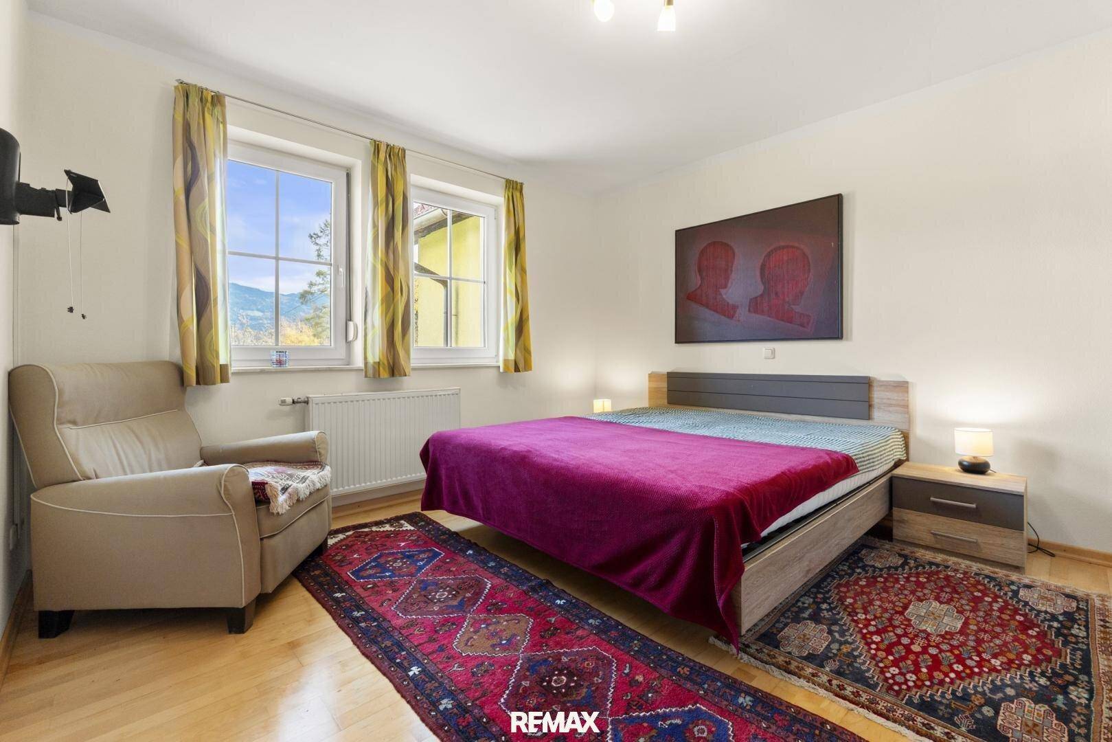 Gemütliches Schlafzimmer mit Holzboden, zwei Fenstern und traditionellen Teppichen.