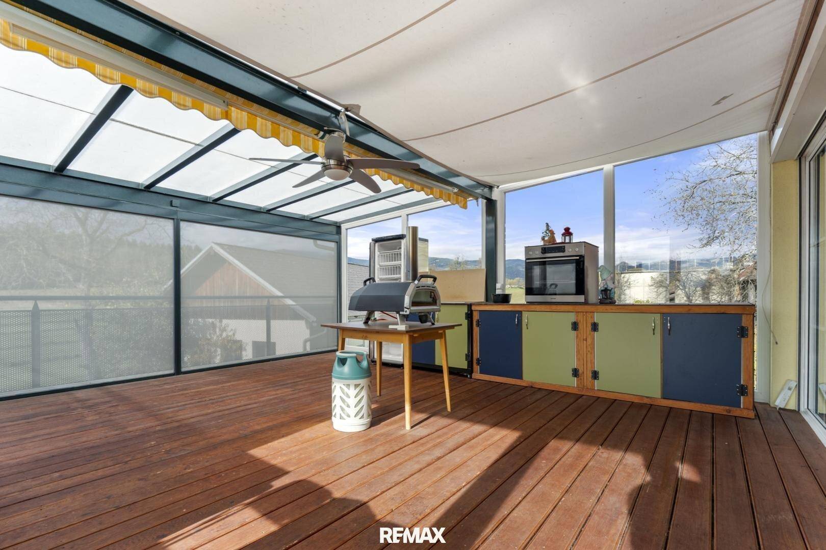 Überdachte Terrasse mit Holzboden, Außenküche und weitem Blick in die umliegende Landschaft.