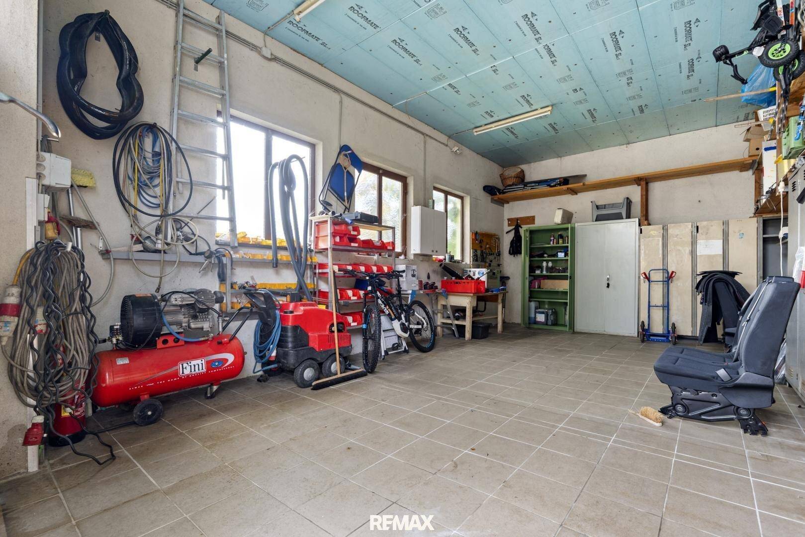 Geräumige Garage oder Werkstatt mit Fliesenboden, Werkzeugen und Geräten.