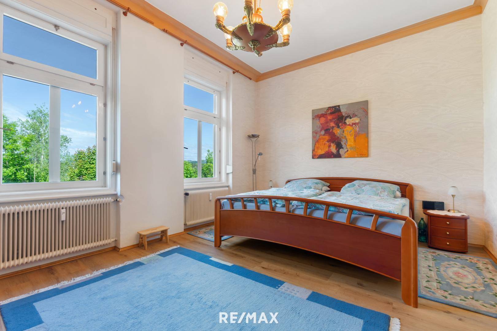 Geräumiges Schlafzimmer mit Holzbett, Parkettboden und großen Fenstern mit grüner Aussicht.