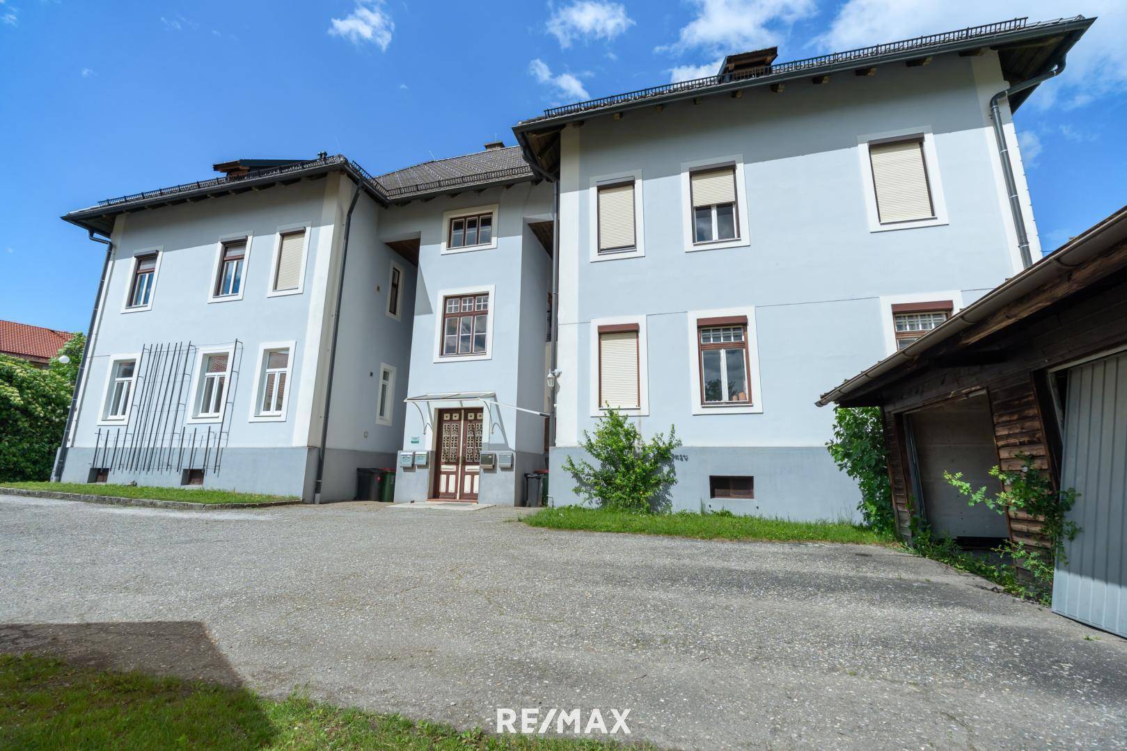 Vorderansicht des historischen Gebäudes mit Eingangsbereich und großzügiger Parkfläche.