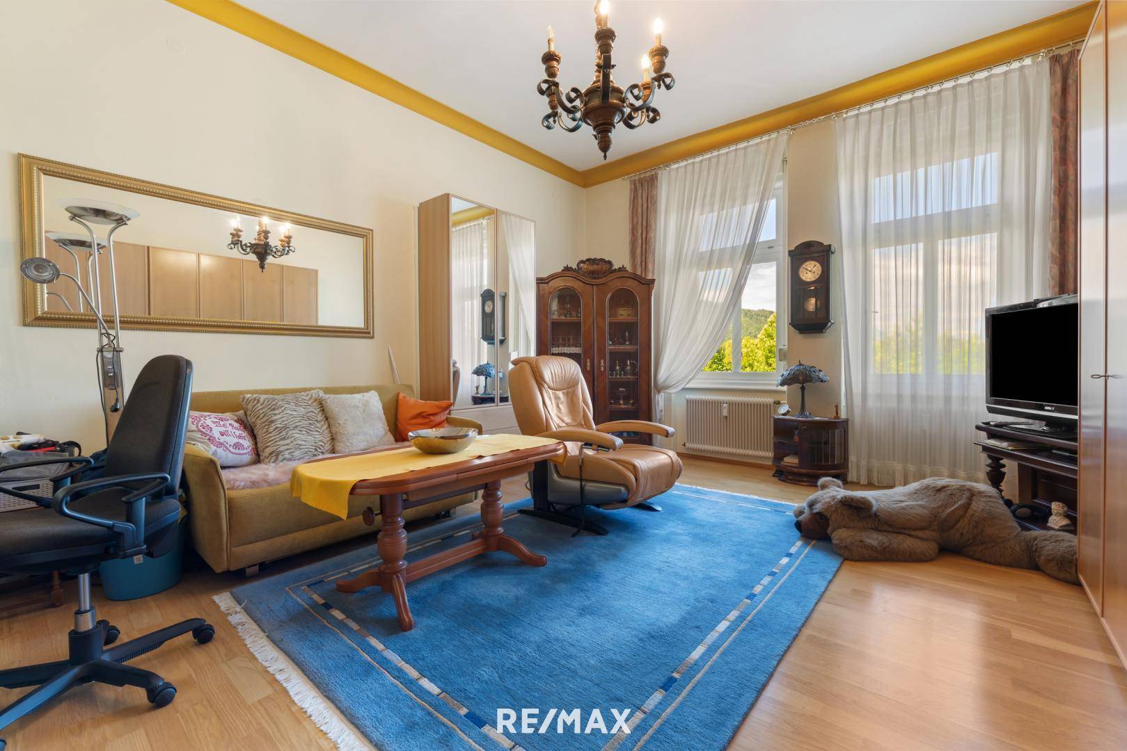 Gemütliches Wohnzimmer mit beigem Sofa, Parkettboden und großem Spiegel, der den Raum erweitert.