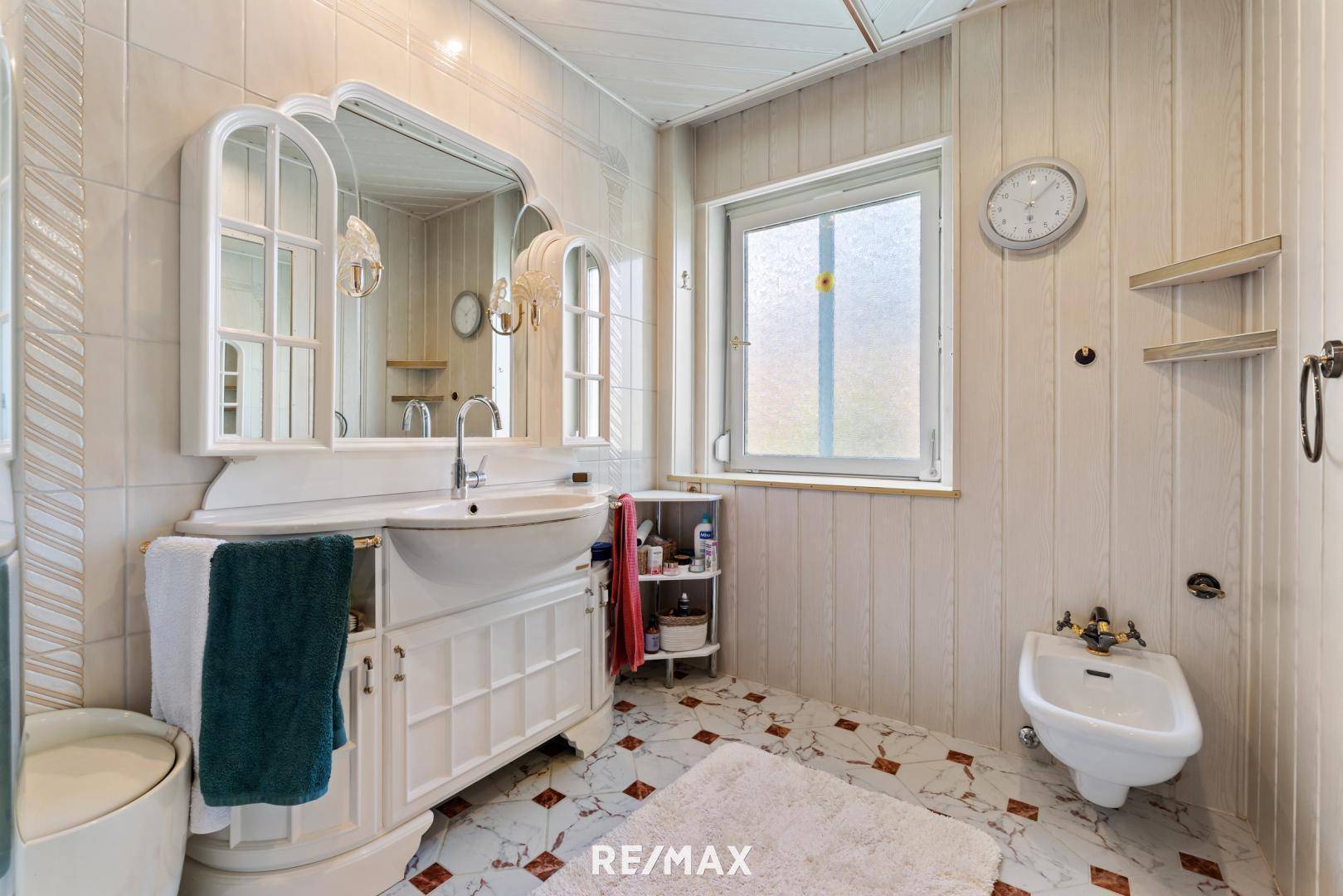 Badezimmer mit Waschtisch, Spiegel und Bidet, hell gefliest und mit Fenster.