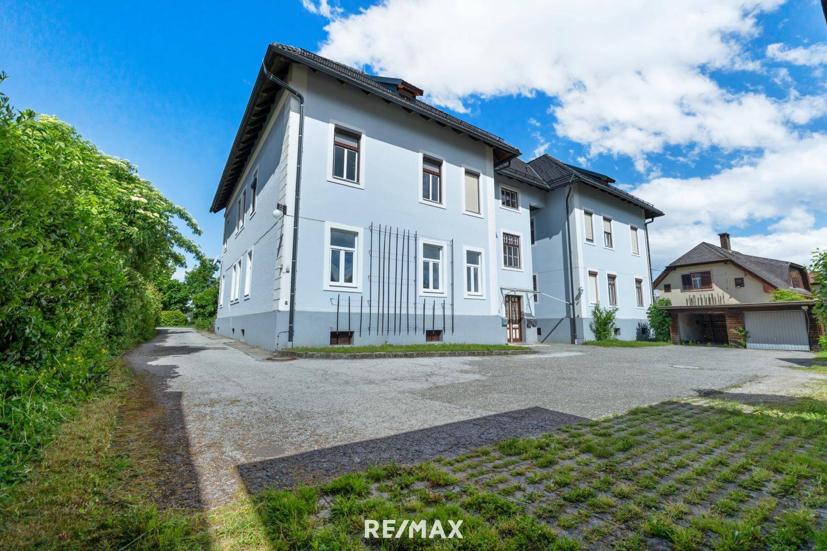 Seitenansicht des Gebäudes mit großem Parkplatz und viel Grün in der Umgebung.