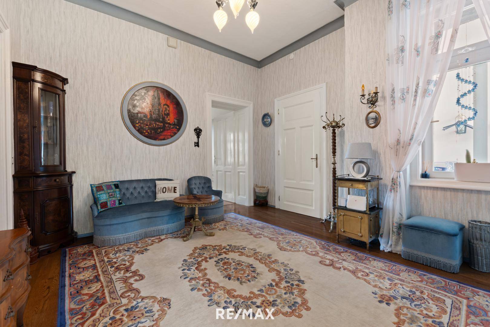 Elegantes Wohnzimmer mit blauer Couch, gemustertem Teppich und hohen Decken.