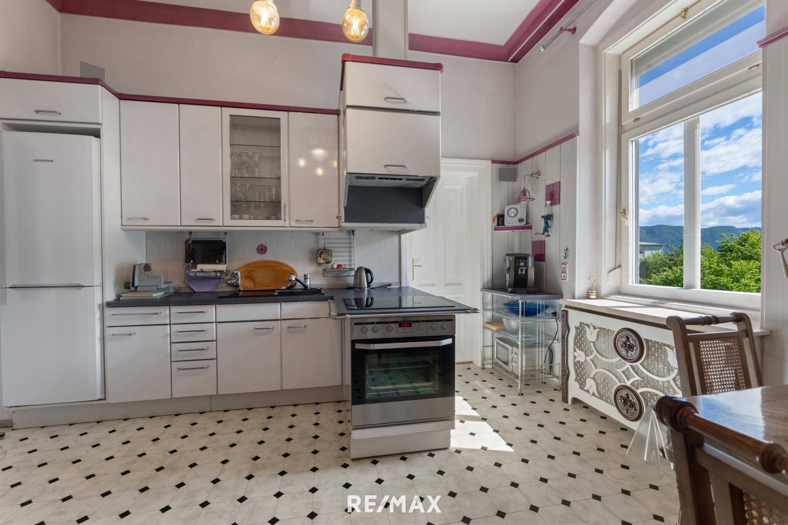 Helle Küche mit weißen Schränken, Fliesenboden und großem Fenster mit Bergblick.