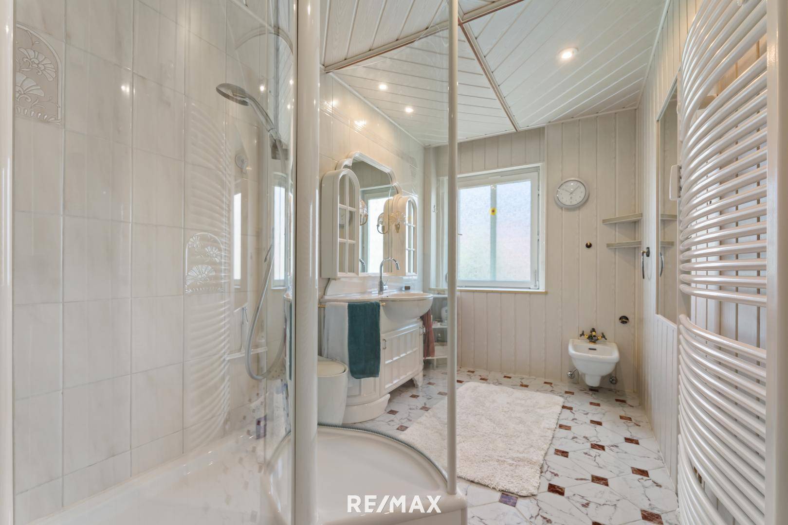 Helles Badezimmer mit Duschkabine, Bidet und Fenster, ausgestattet mit weißen Fliesen.