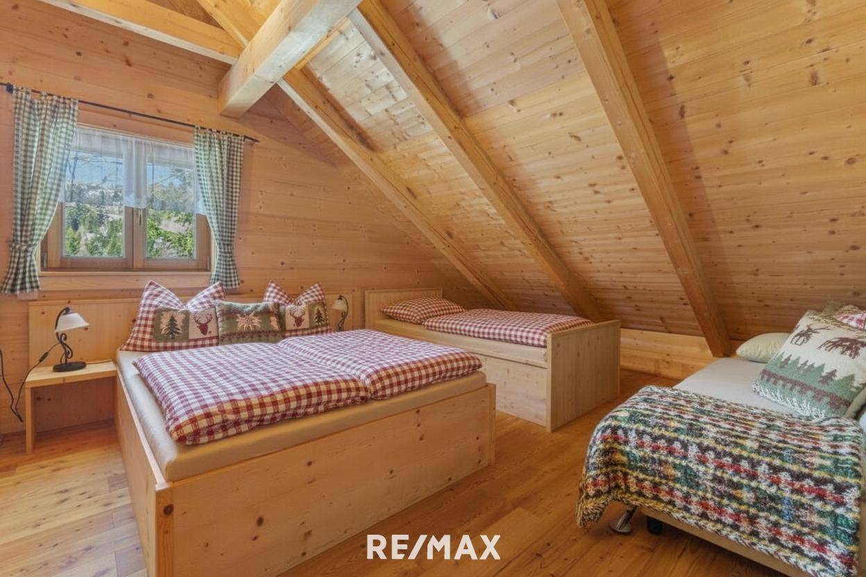 Helles Schlafzimmer im Dachgeschoss mit Holzbalken, mehreren Betten und Blick auf die umliegende Natur.