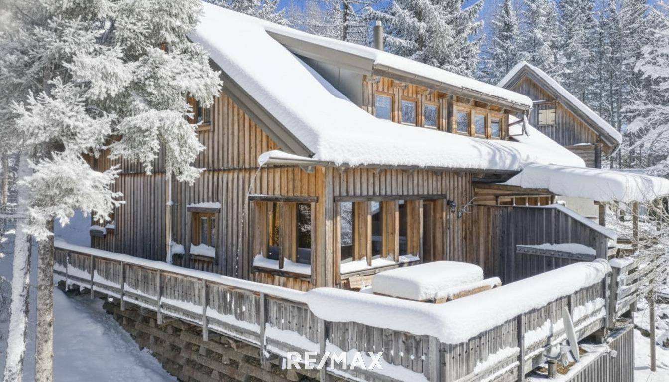Charmantes Holzchalet, vollständig mit Schnee bedeckt, umgeben von verschneiten Tannenbäumen in alpiner Umgebung.