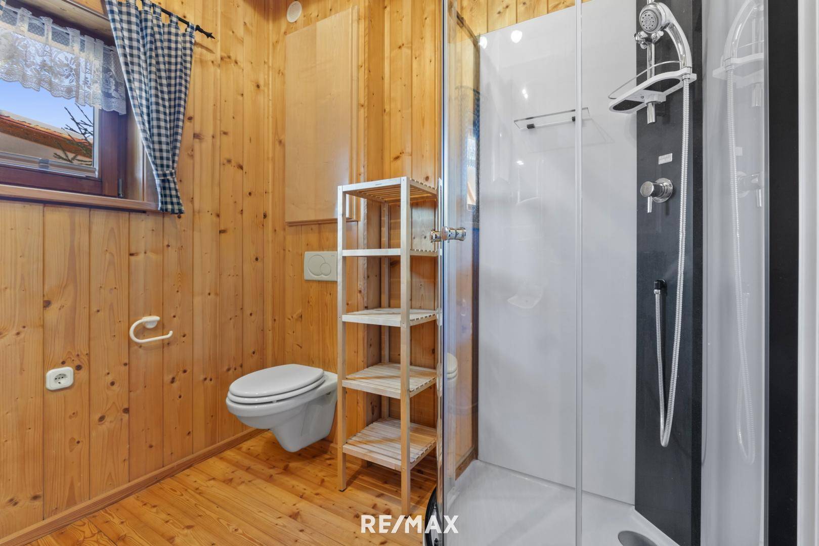 Badezimmer mit Holzverkleidung, Toilette und moderner Duschkabine, gut beleuchtet durch ein Fenster.