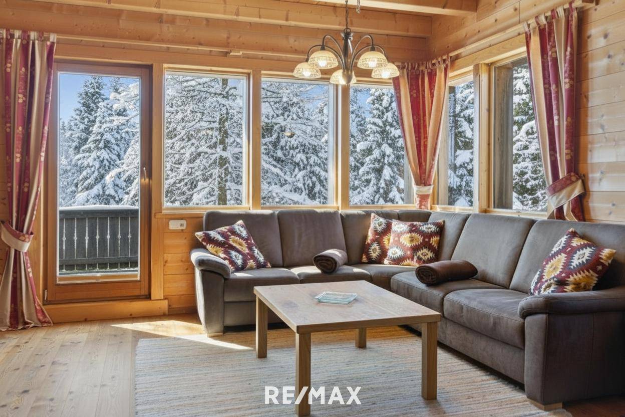 Helles Wohnzimmer mit großem Sofa, Holztisch und Zugang zum Balkon mit Blick auf die verschneiten Wälder.