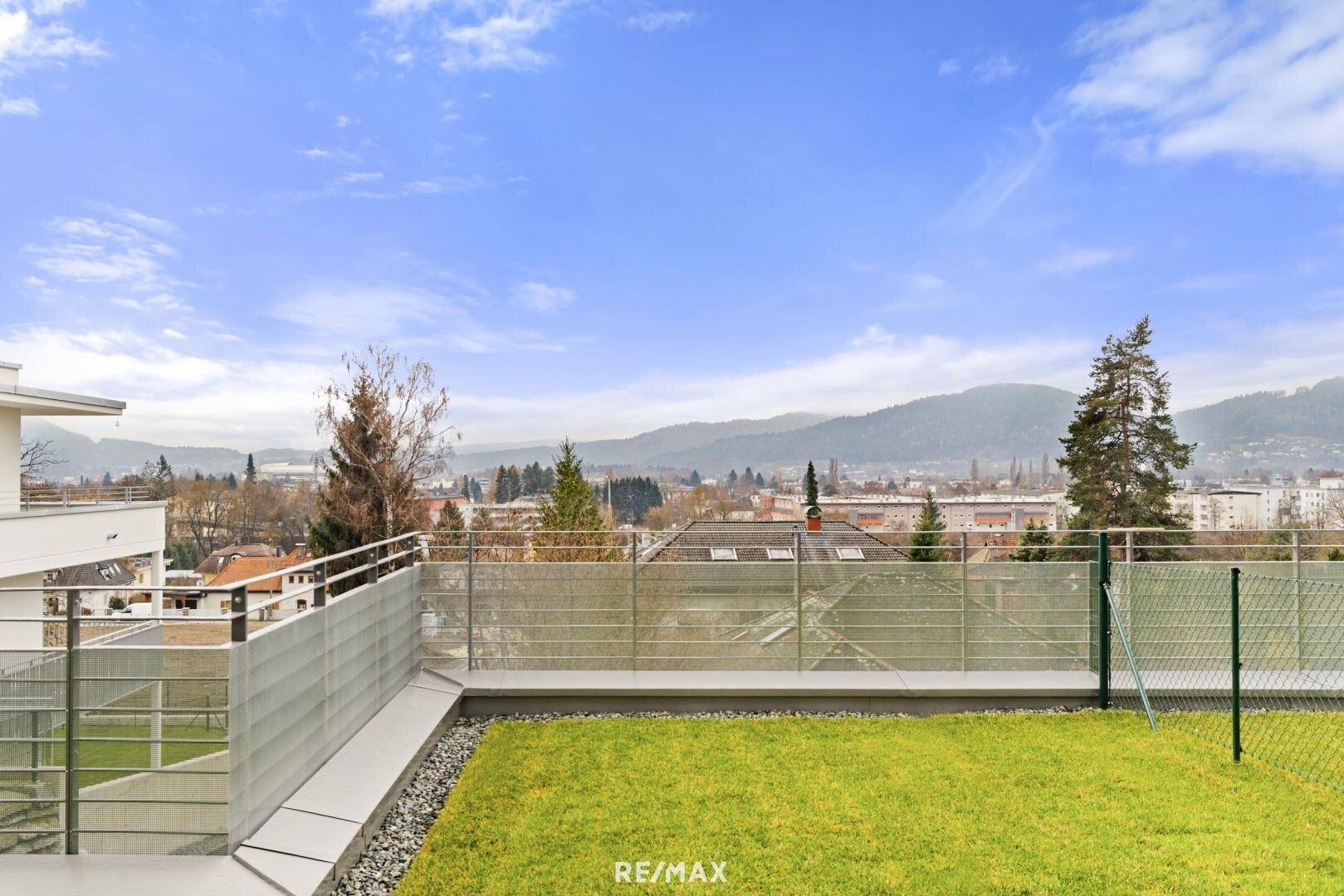 Grüne Rasenfläche mit moderner Umzäunung und weitem Blick über die Stadt und die Berge.