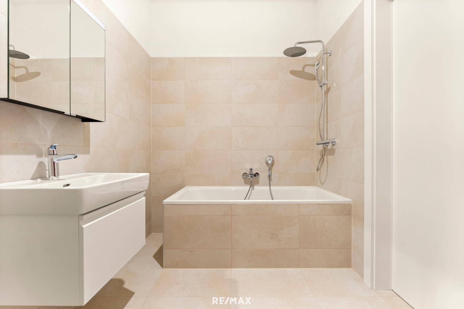 Helles Badezimmer mit Badewanne, Dusche und modernem Waschtisch, gefliest in warmen Beigetönen.