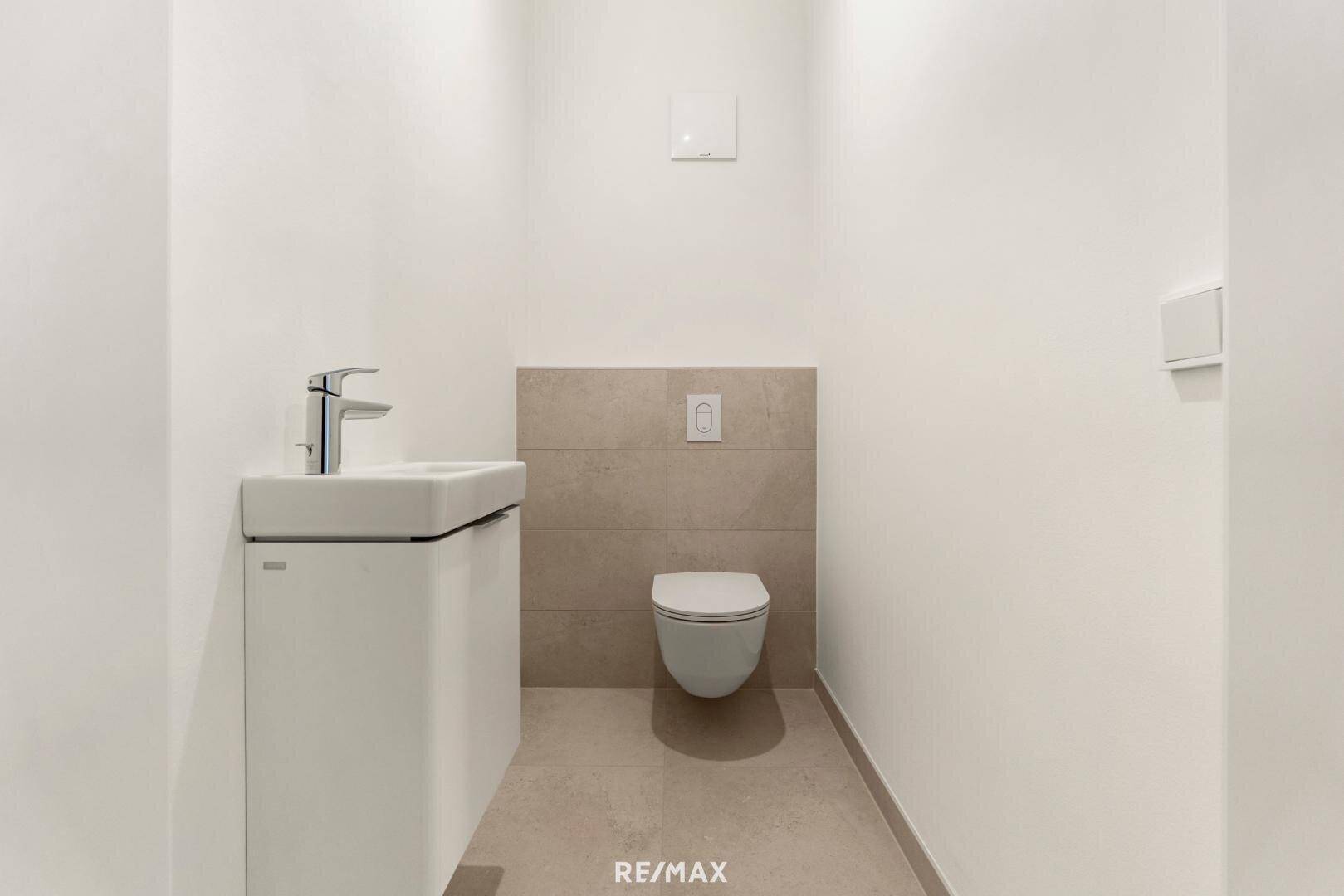 Modernes Gäste-WC mit wandhängendem WC und kleinem Waschbecken, in neutralen Farbtönen gehalten.