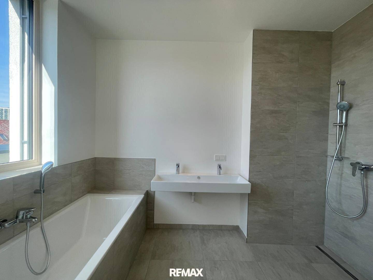Helles Badezimmer mit Badewanne, Doppelwaschbecken, begehbarer Dusche und Fenster für Tageslicht.