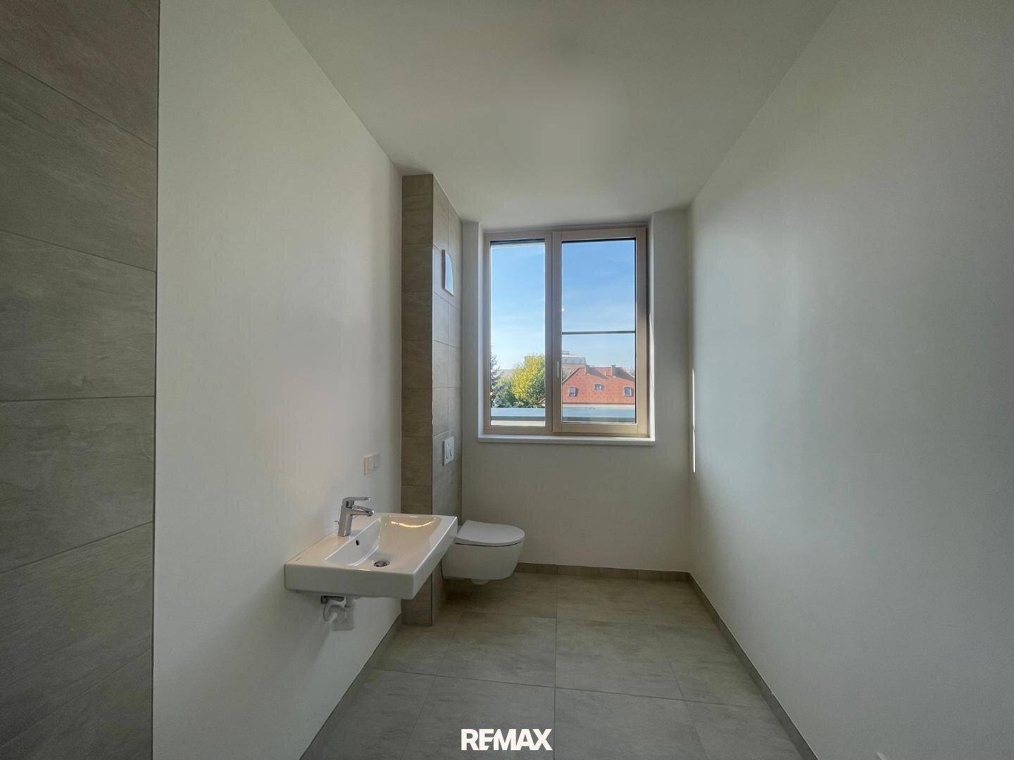 Separates WC mit wandhängender Toilette, kleinem Waschbecken und Fenster für Belüftung.