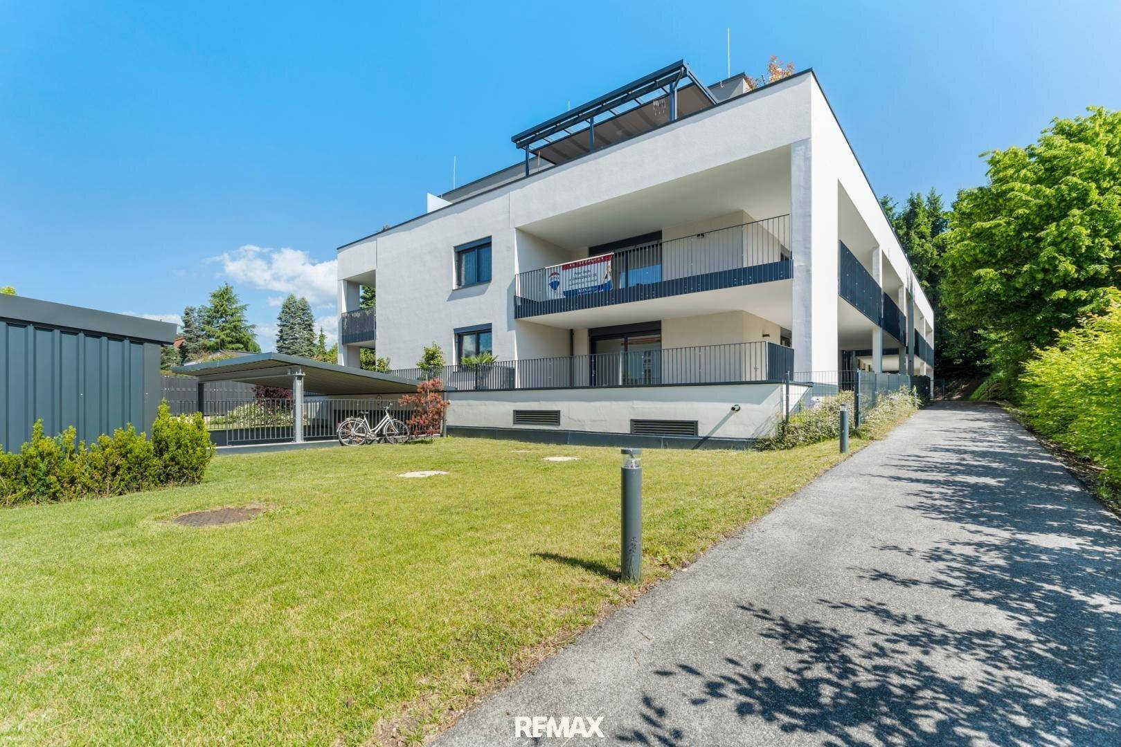 Modernes Mehrfamilienhaus mit Balkonen, Grünfläche und Carport im Außenbereich.