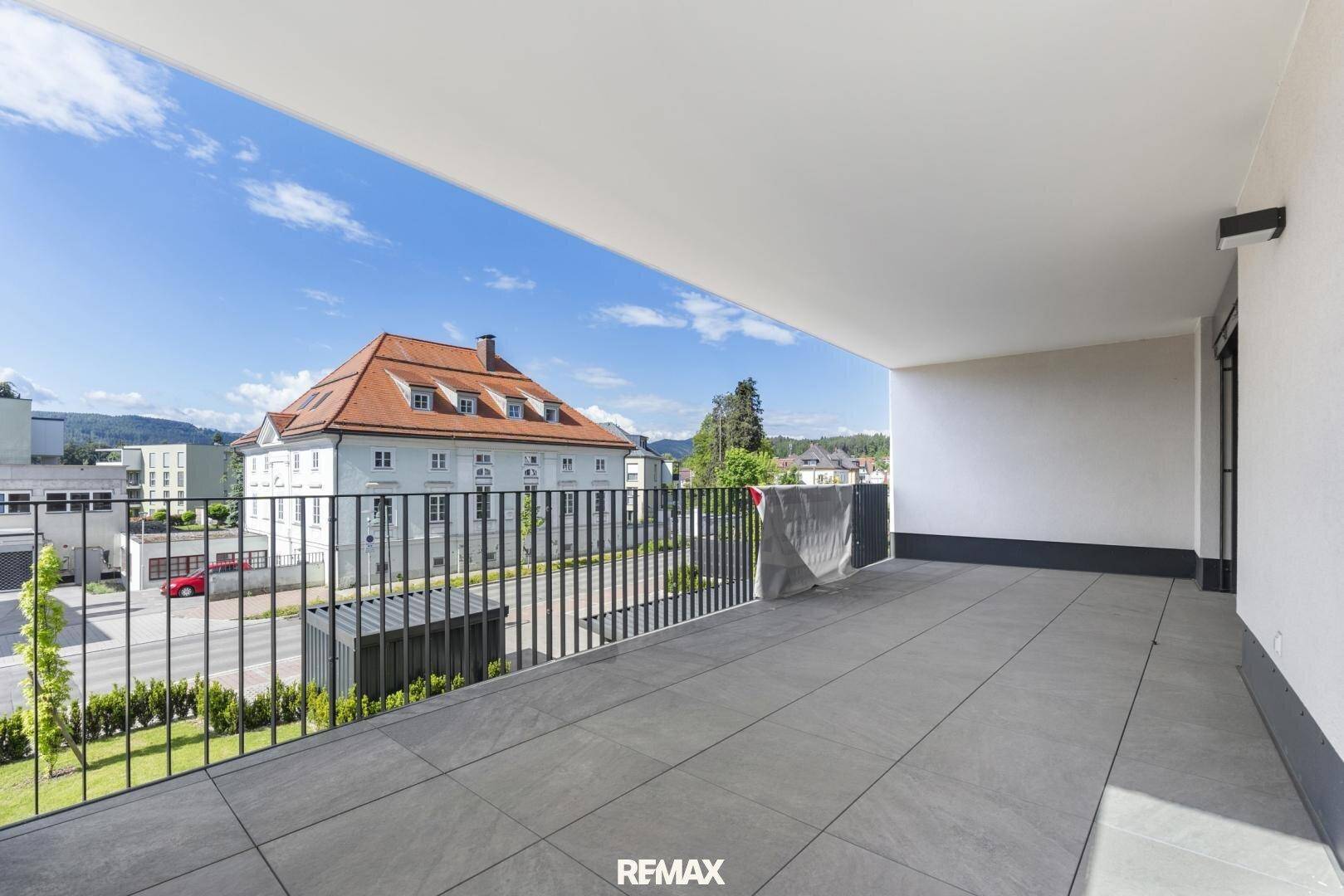 Geräumiger Balkon mit grauen Fliesen und Blick auf die umliegenden Gebäude und die Stadt.