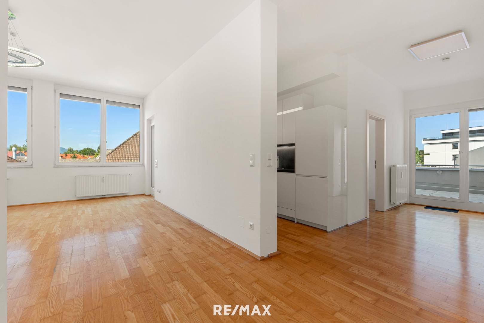 Heller Wohnbereich mit Parkettboden, großen Fenstern und Zugang zu einem Balkon oder einer Terrasse.