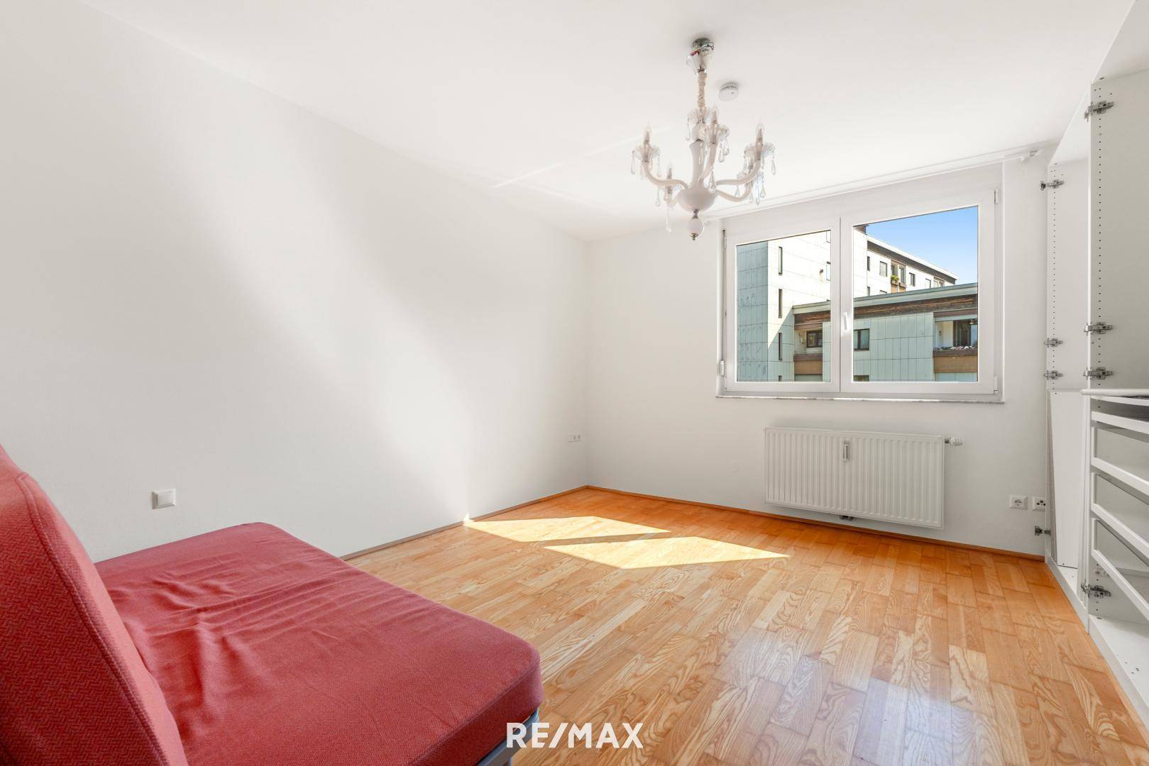 Helles Schlafzimmer mit Parkettboden, Fenster und einem dekorativen Kronleuchter sowie Einbauschränken.