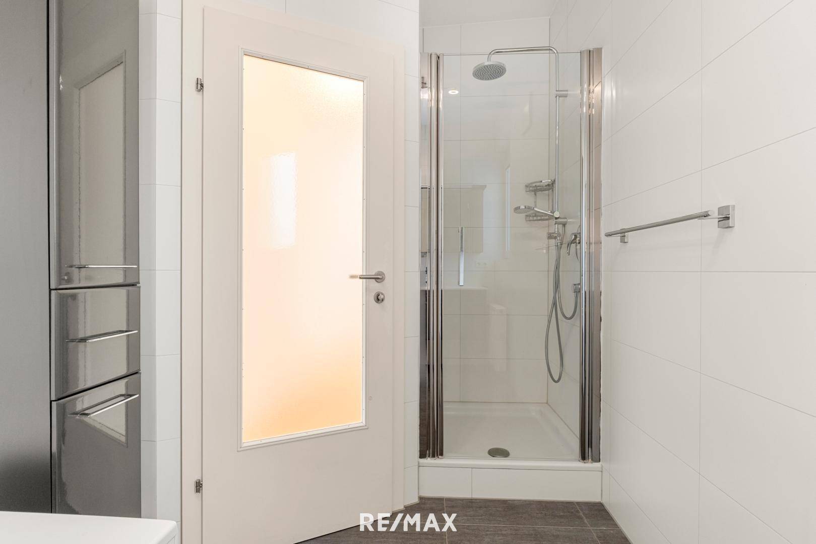 Modernes Badezimmer mit Duschkabine und weißen Fliesen, ausgestattet mit einer Regendusche.