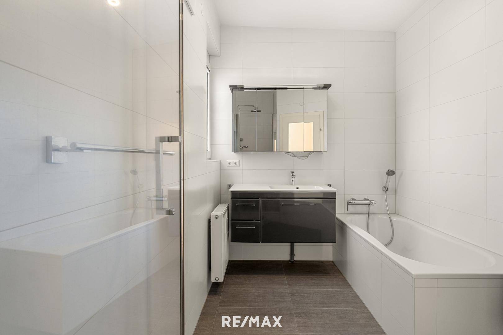 Modernes Badezimmer mit Badewanne, Waschtisch und Spiegelschrank, komplett gefliest.