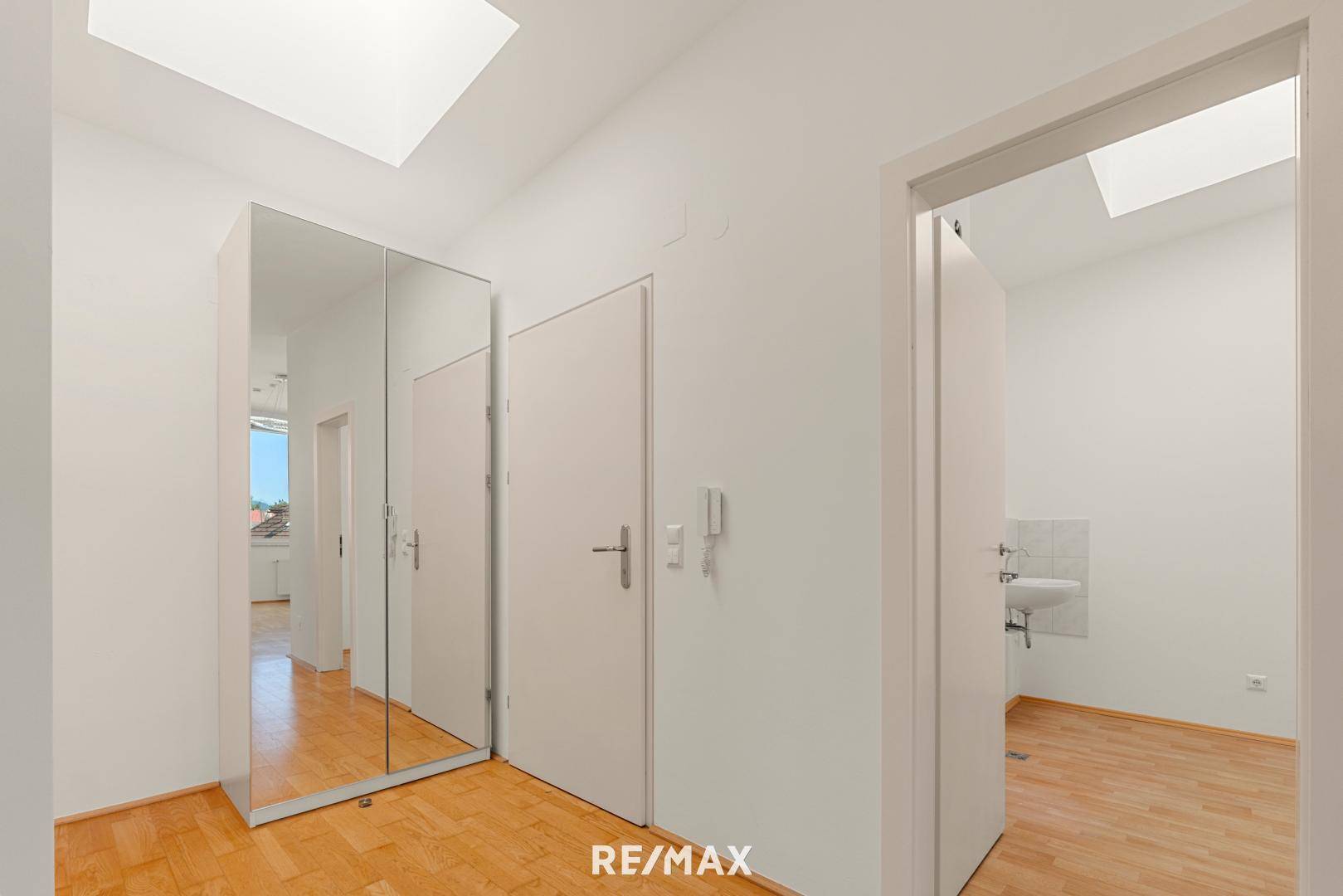 Heller Flur mit Parkettboden, Spiegelschrank und Zugang zu verschiedenen Räumen.