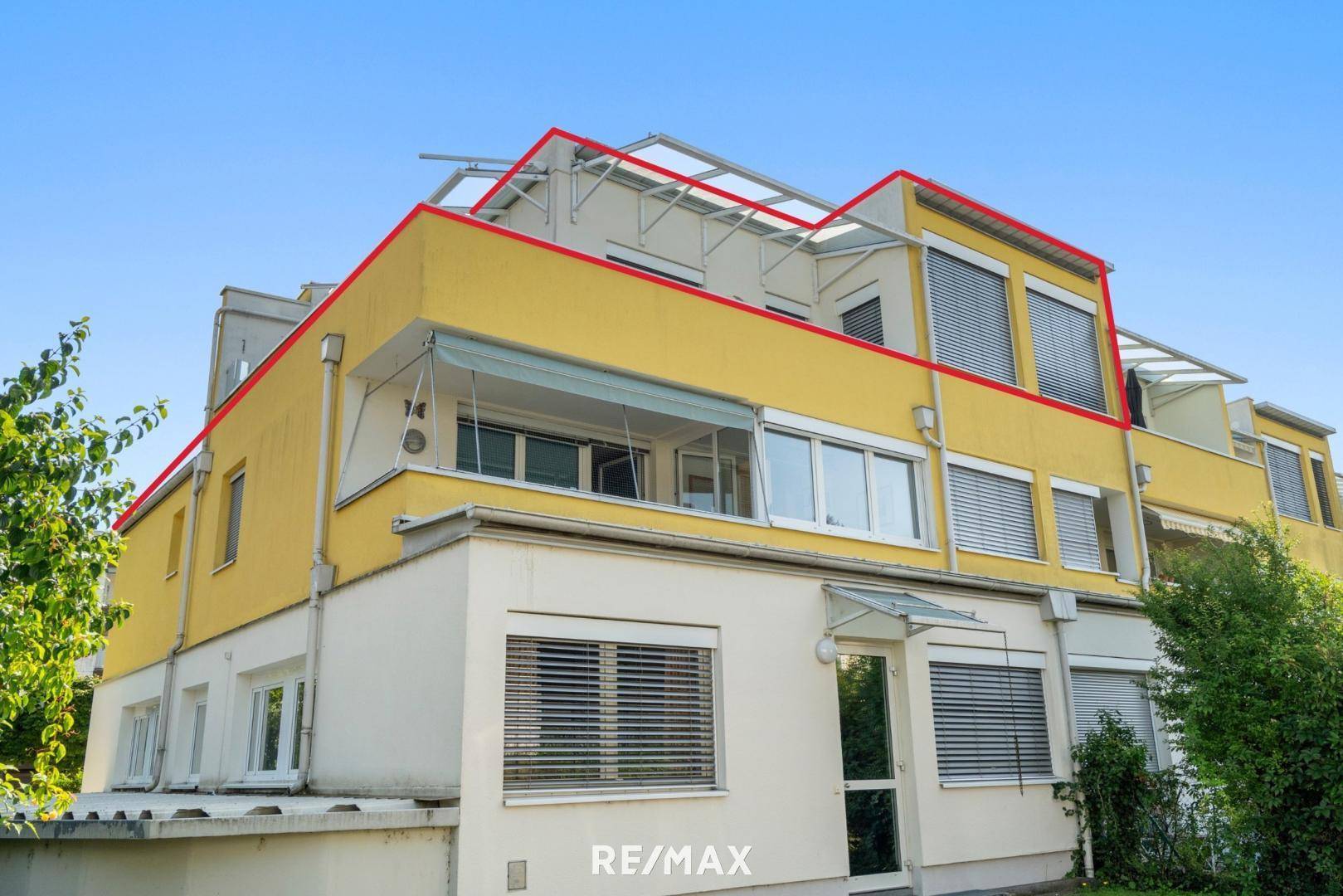 Seitenansicht des gelben Gebäudes mit Balkonen und Terrassen, die zum Verkauf stehende Einheit ist markiert.