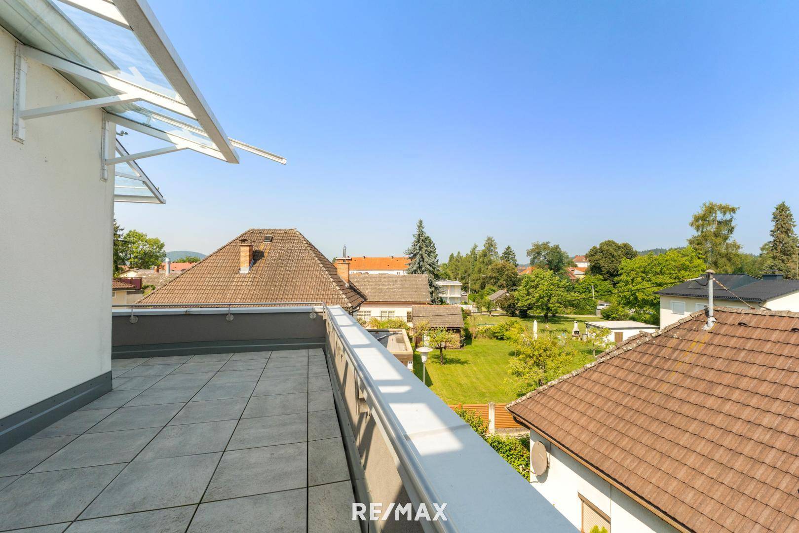 Sonniger Terrassenbereich mit Fliesenboden und Ausblick auf die Dächer der Nachbarschaft und grüne Hügel.
