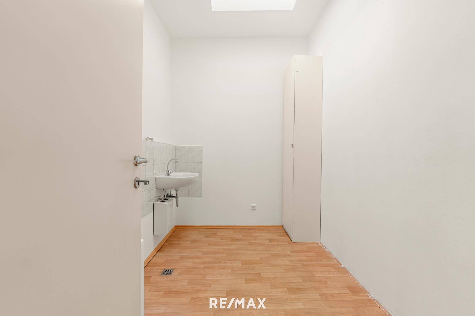 Praktischer Hauswirtschaftsraum mit kleinem Waschbecken, Parkettboden und einem Oberlicht.