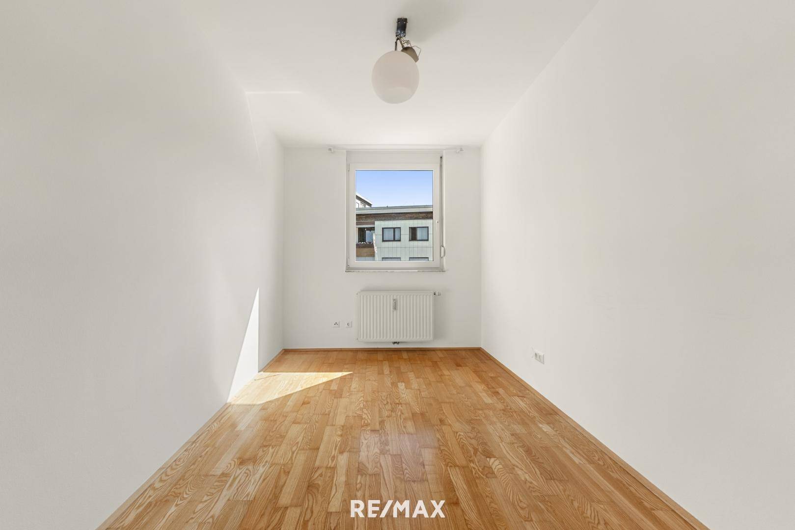Leeres, helles Zimmer mit Parkettboden und einem Fenster, das viel Tageslicht bietet.