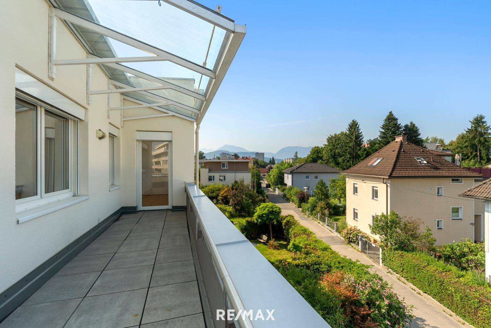 Lange, geflieste Terrasse mit Glasüberdachung und weitem Blick über die grüne Umgebung.