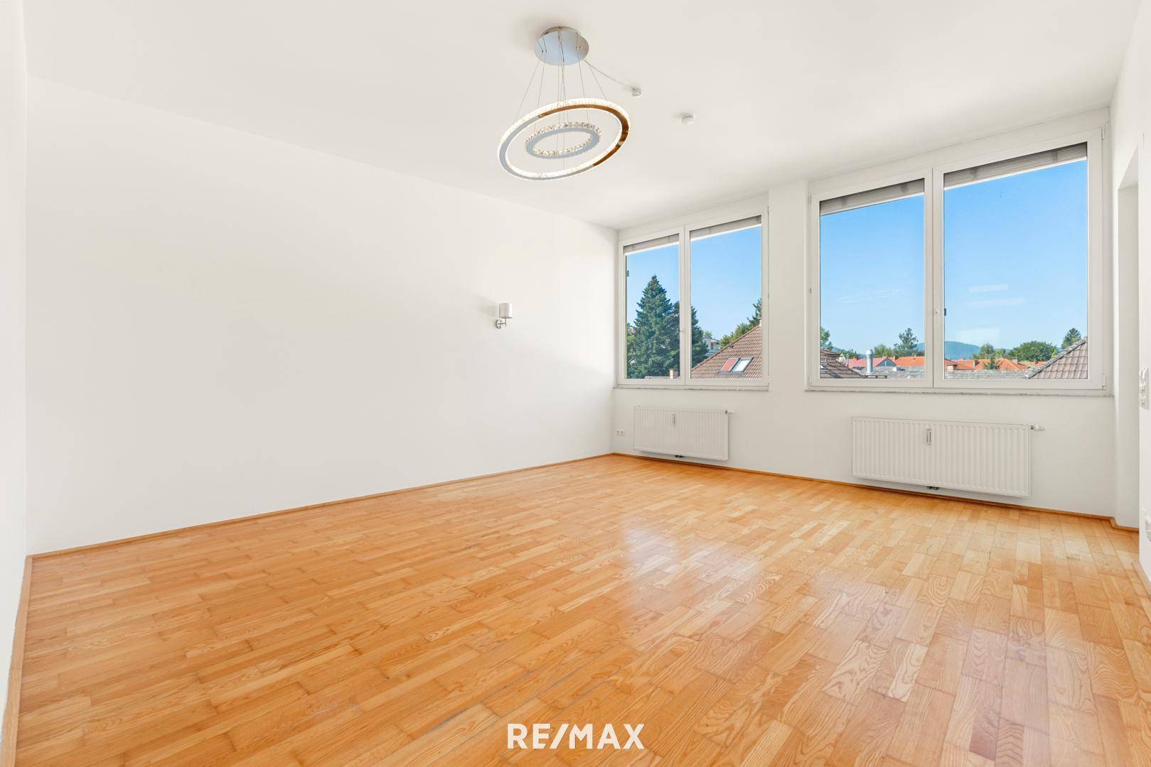 Geräumiger, heller Wohnraum mit Parkettboden und großen Fenstern, die viel Tageslicht hereinlassen.