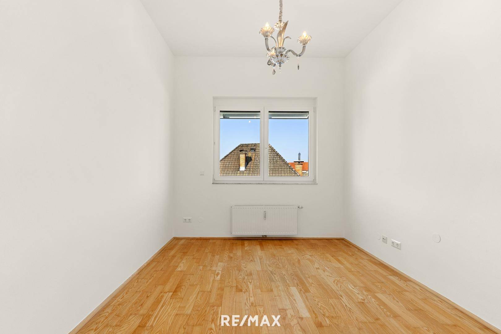 Helles Zimmer mit Parkettboden und einem Fenster mit Blick auf die umliegenden Dächer.