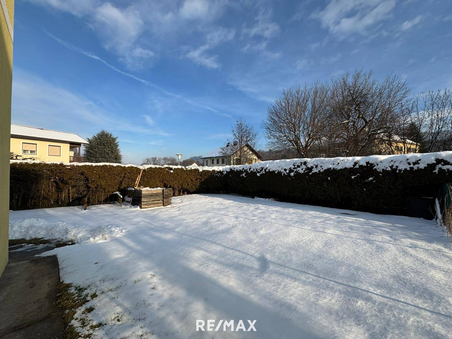 Verschneiter Gartenbereich mit hoher Hecke und Bäumen im Hintergrund während der Winterzeit.