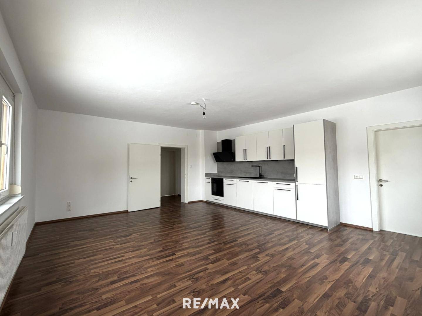 Weitläufiger Wohnraum mit moderner Küchenzeile und Zugang zu weiteren Zimmern.