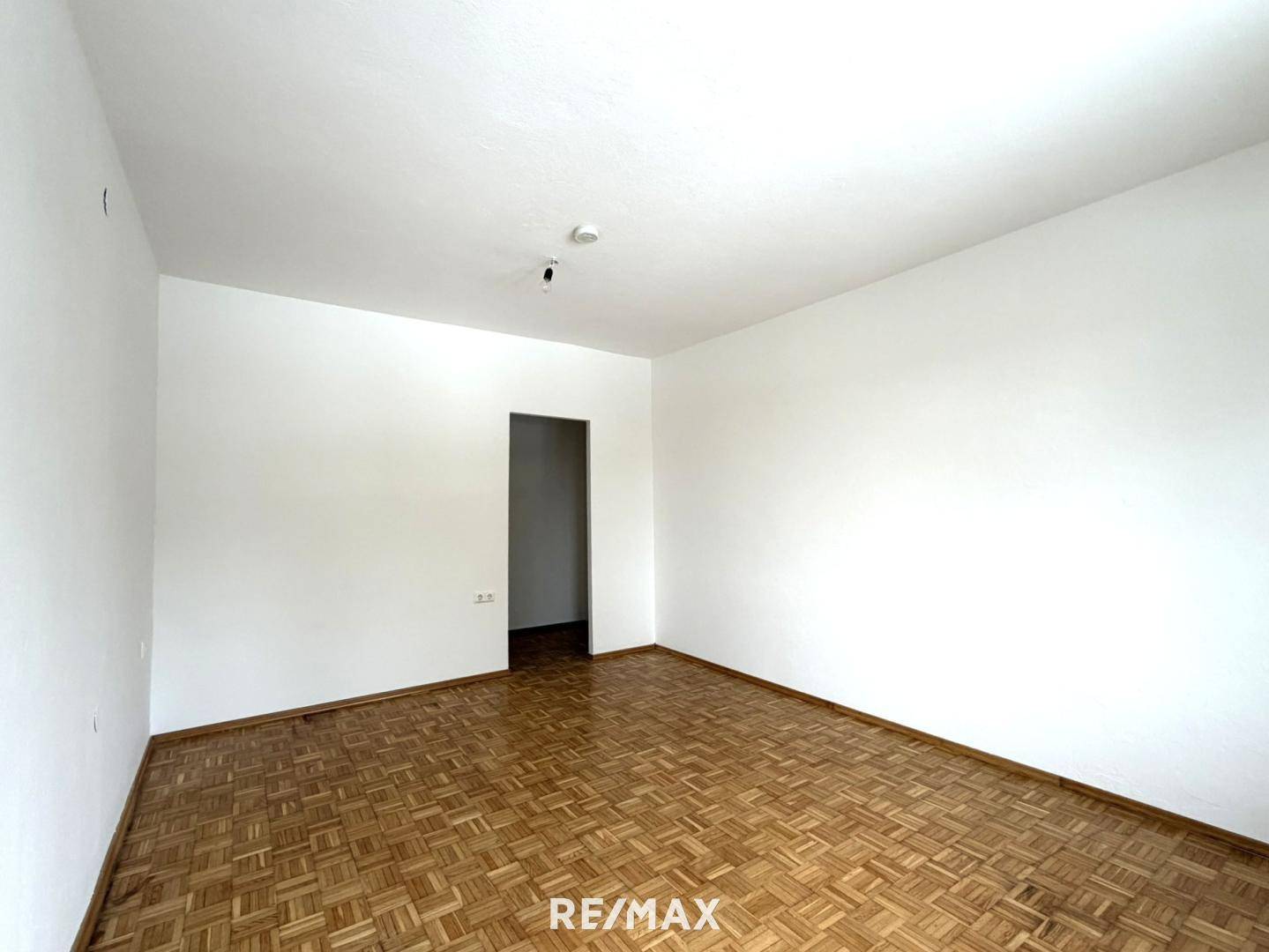 Leeres Zimmer mit klassischem Parkettboden und weiß gestrichenen Wänden.