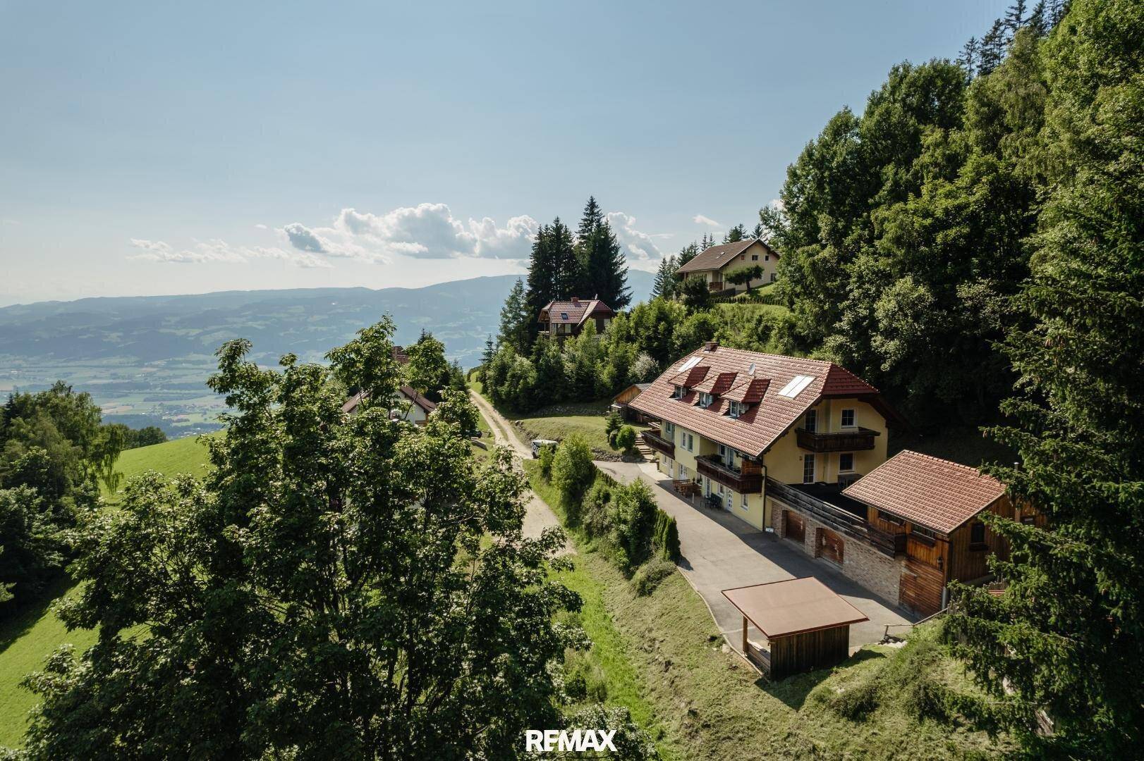 Malerische Luftaufnahme eines Anwesens am Hang, umgeben von grünen Bäumen mit weitem Ausblick.