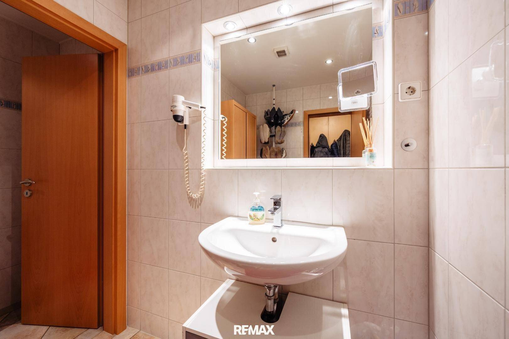 Badezimmer mit hellen Fliesen, Einzelwaschbecken, großem Spiegel und Holzdetails.