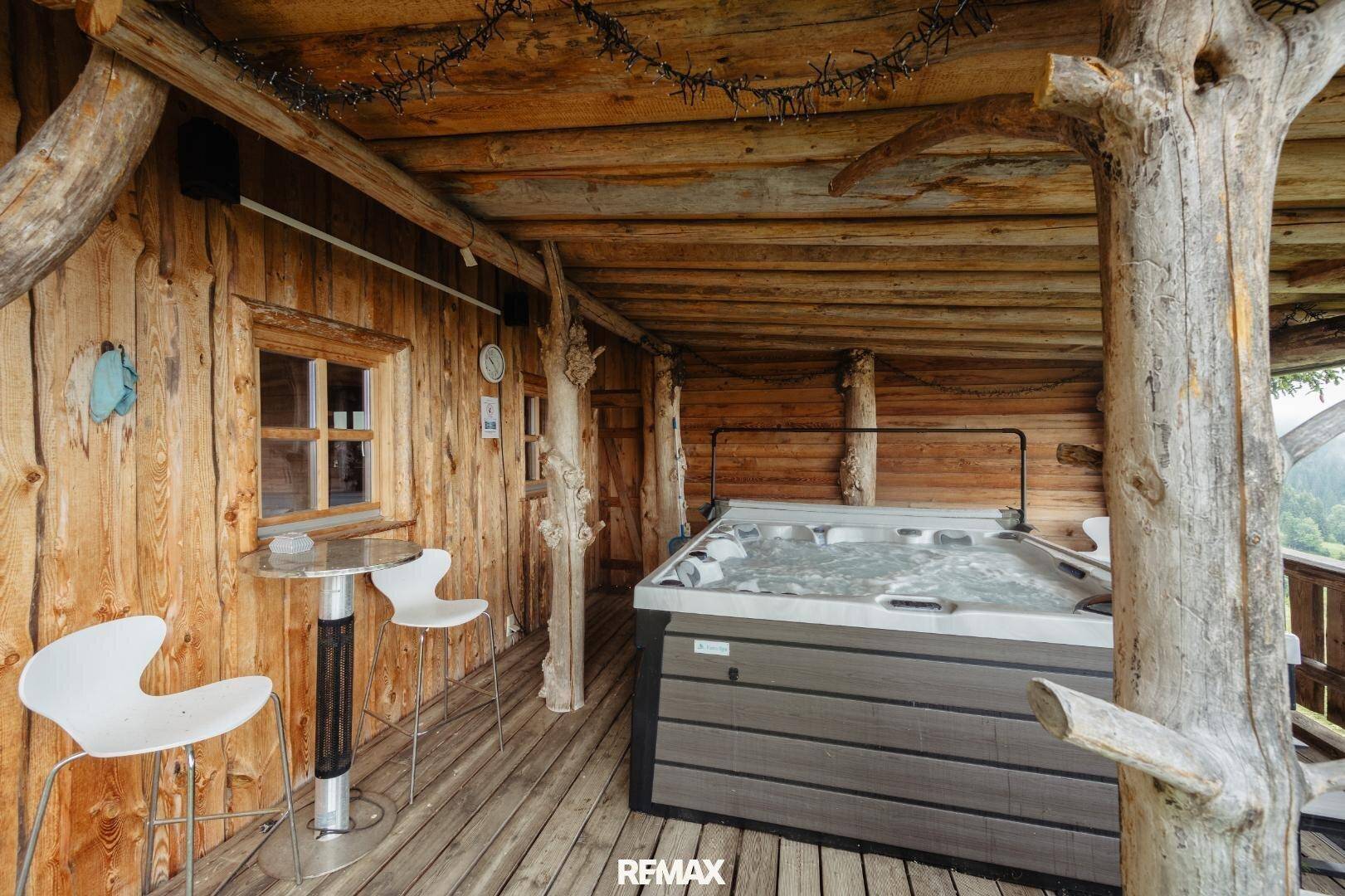 Überdachte Holzterrasse mit Whirlpool und Sitzgelegenheiten, ideal zum Entspannen im Freien.