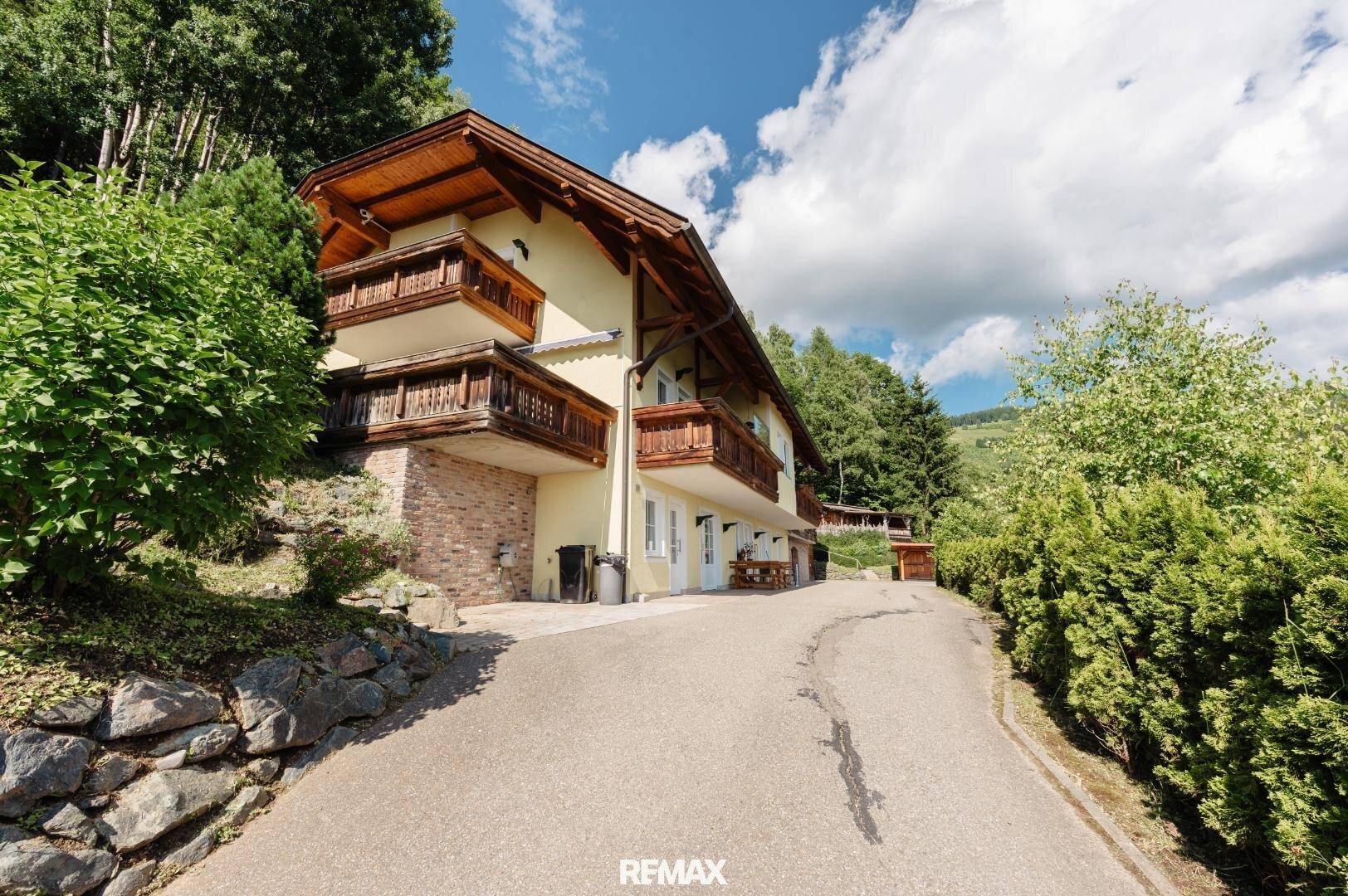 Charmantes Haus im alpinen Stil mit Holzbalkonen und einer Auffahrt, umgeben von viel Grün.