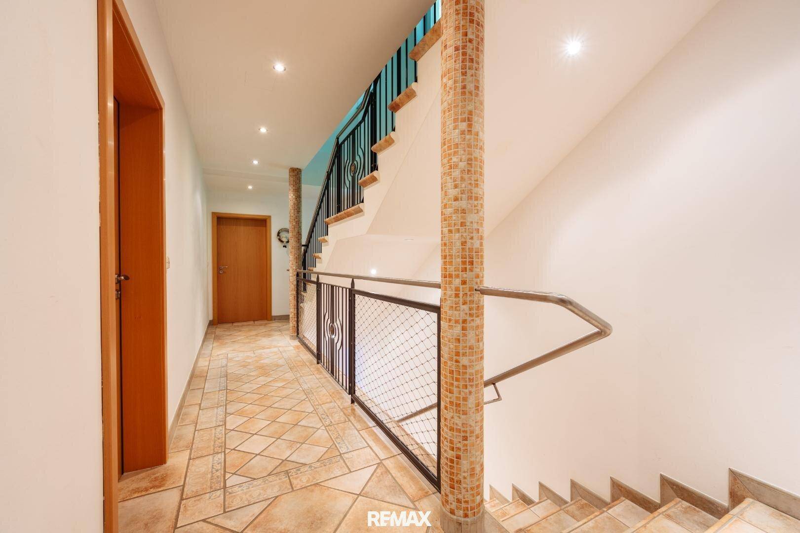 Heller Flur mit gefliestem Boden, Treppe und dekorativen Säulen, die zum Obergeschoss führen.