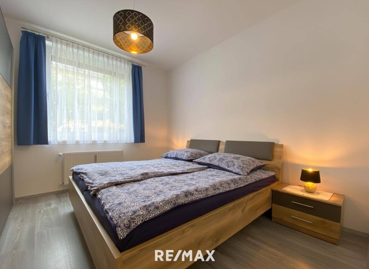 Schlafzimmer mit Doppelbett, Nachttisch und Fenster mit blauen Vorhängen.