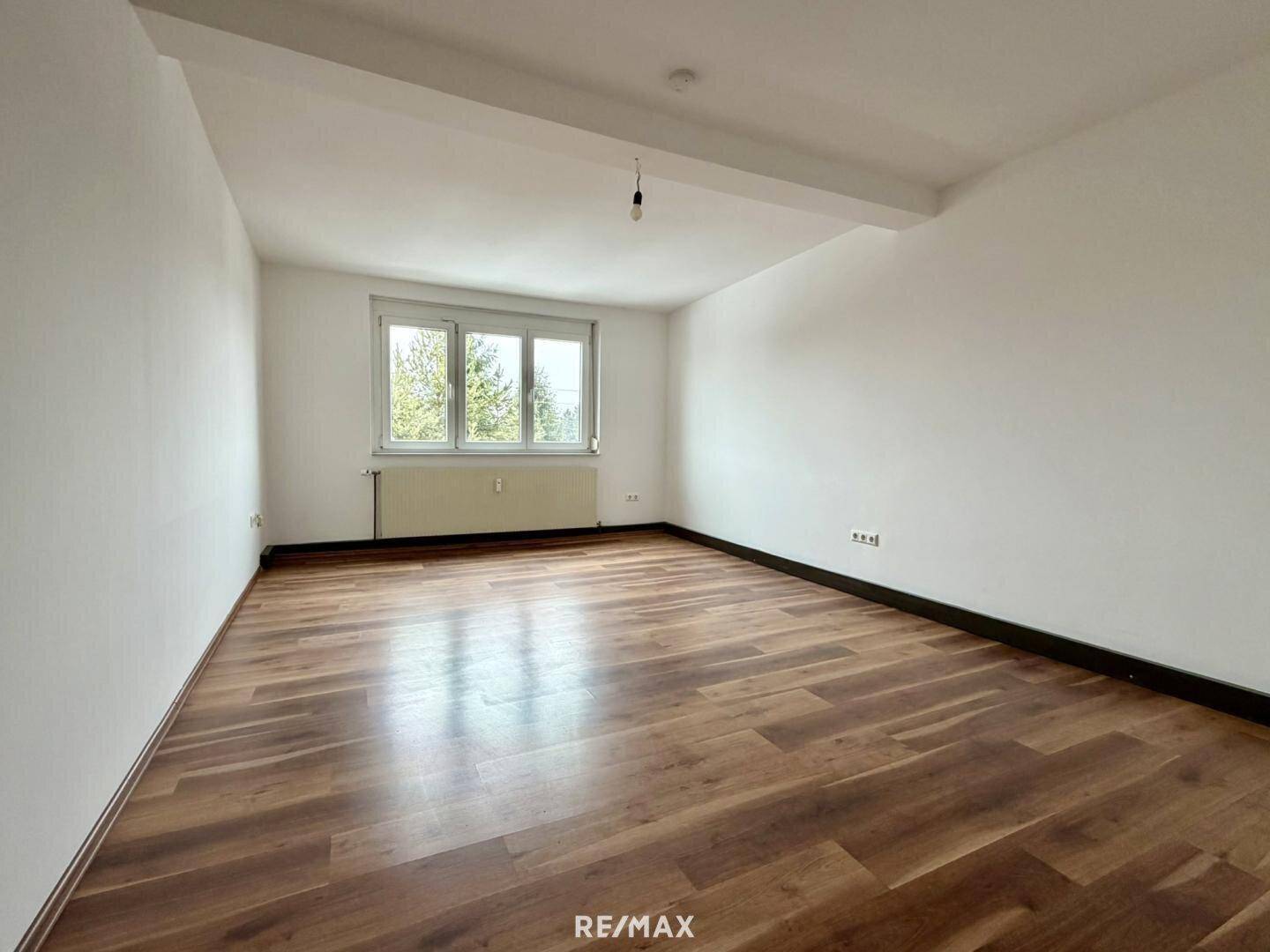 Geräumiges Wohnzimmer mit großen Fenstern, Laminatboden und viel Tageslicht.