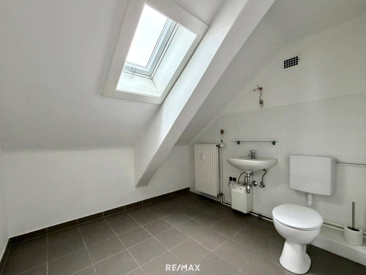 Kleines WC im Dachgeschoss mit Dachfenster, Fliesenboden, Toilette und Waschbecken.