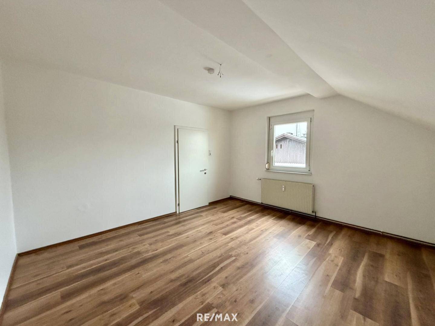 Leeres Zimmer im Dachgeschoss mit Laminatboden, schräger Decke und Fenster.