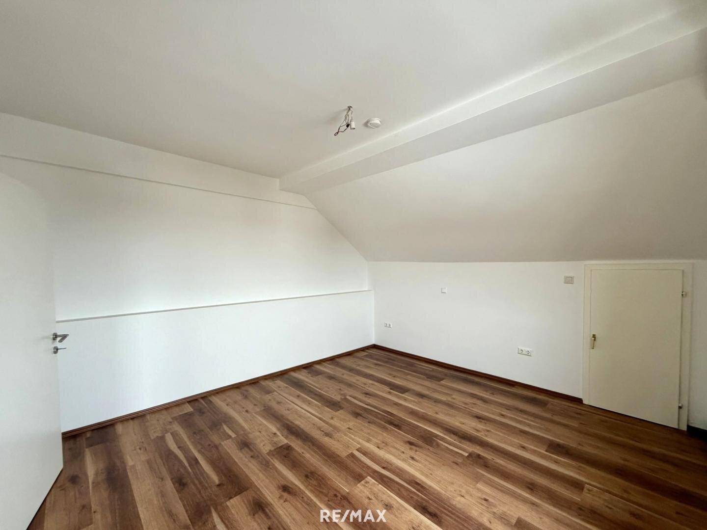 Unmöbliertes Zimmer im Dachgeschoss mit Laminatboden und schräger Decke.