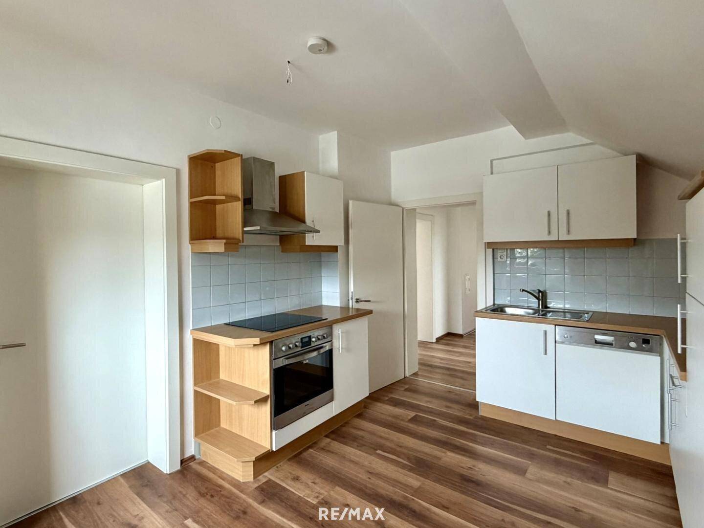 Funktionale Einbauküche mit weißen Schränken, Induktionskochfeld und Laminatboden im Dachgeschoss.